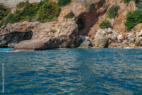 Steep stone coast of the Mediterranean Sea in Alanya (Turkey) - view from the water. Beautiful seascape with turquoise blue water, brown rocks and boulders on the shore and green plants on the slopes