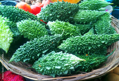 Heap of fresh green bitter gourd vegetables in a wicker basket for selling on the market. photo