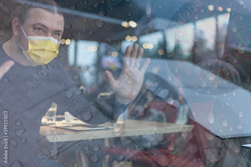 Businessman with a medical mask at the time of the covid pandemic, working on a laptop in a public place on a rainy day outside