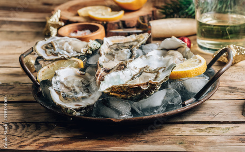 Oysters with lemon on a vintage dish on a rustic wooden background with a festive decor. Christmas dinner.