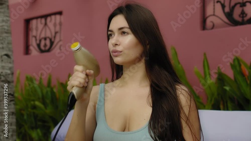 Wallpaper Mural European girl in a swimsuit using an electric device for leg skin care like a gun in the backyard sitting on the sunbed near swimming pool Torontodigital.ca