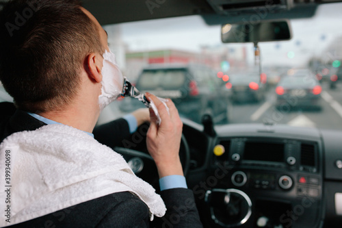 Businessman shaving in car by razor and foam at the wheel. Shaving man in the driver's seat. Hurring. Bluer collar office employee shaveing himself in heavy traffic jam.Beautiful Man in suit