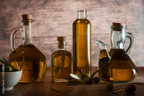  Bottles of extra virgin olive oil, bowl with olives, olive leaves and olives scattered on wooden table. Wooden background.