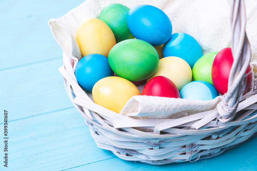 Naklejka premium basket with colorful Easter eggs on a blue wooden background, selective focus, tinted image