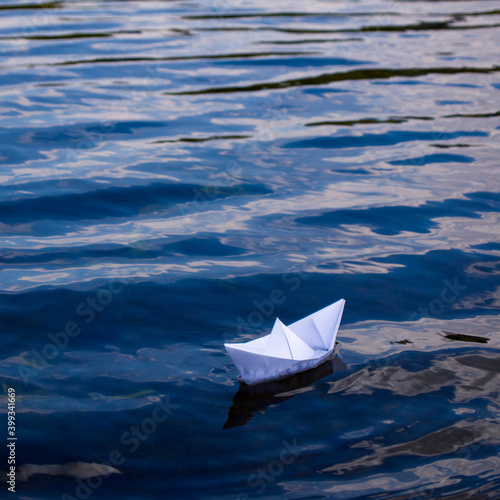 White paper boat in blue water. Origami ship sailing on the river. The concept of movement in the future and achieve the goal. Square format. Copy space. 