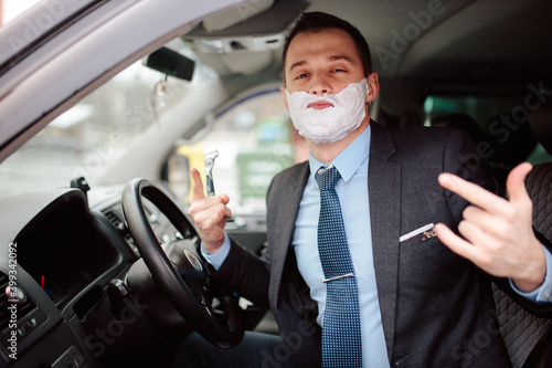 Photography Businessman shaving in car by razor and foam at the wheel