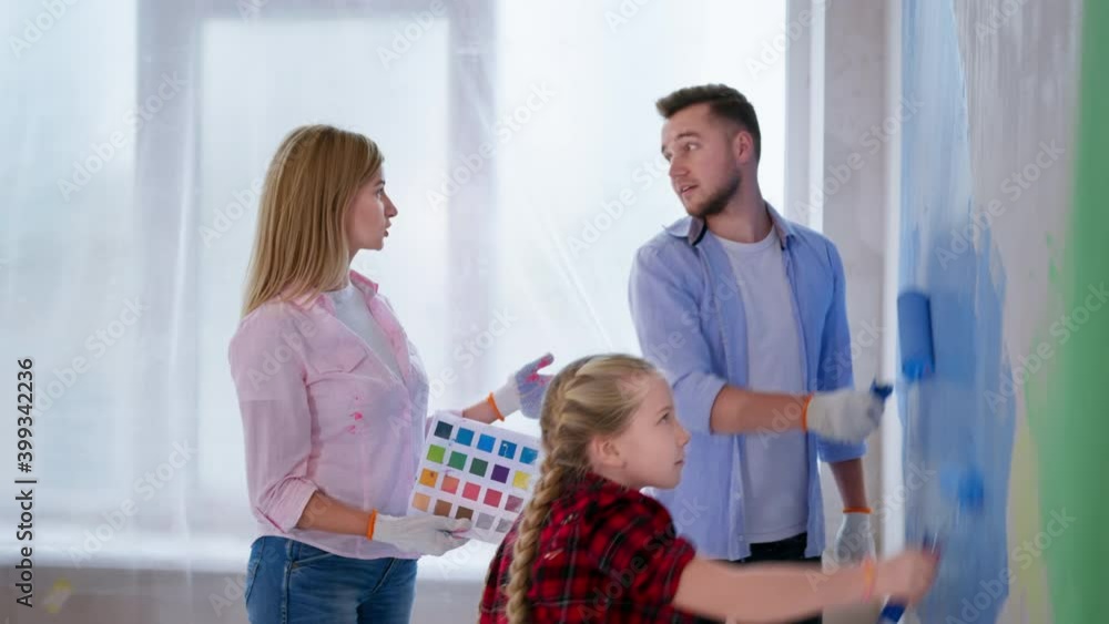 family time together with daughter during apartment renovation, couple and kid girl paint the wall in blue color with rollers in new house
