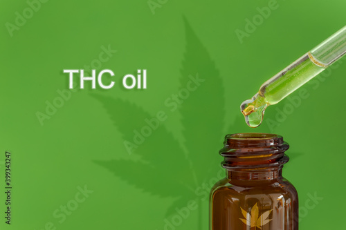 Dropping THC oil on a bottle on a green background. A leaf casts shadow behind.