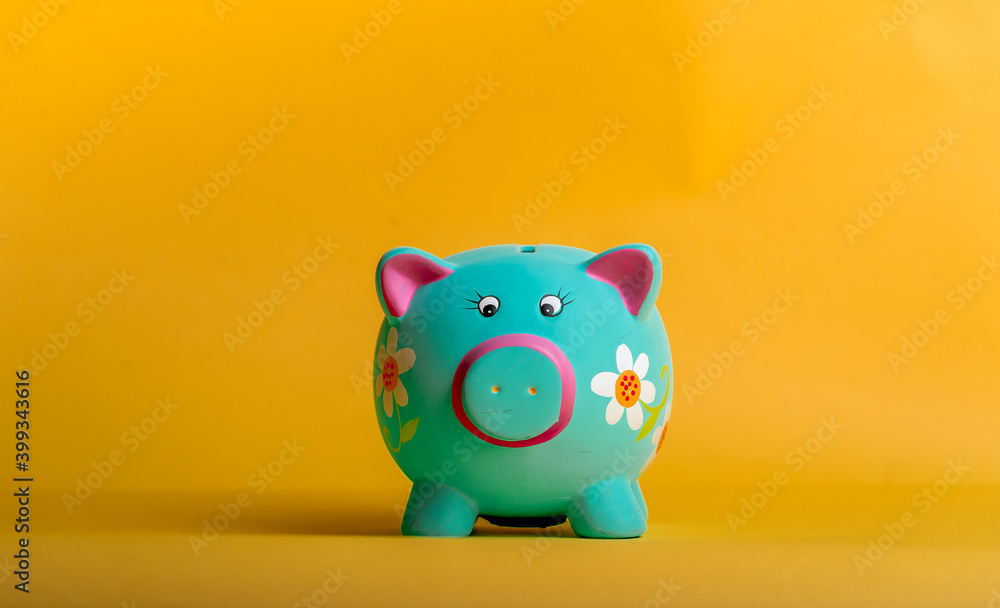 Blue piggy bank in flowers isolated on yellow background, Funny bank for kid savings. Financial education for children. The figure of money savings and investing Blue piggy bank in flowers isolated on yellow background, Funny bank for kid savings. Financial education for children. The figure of money savings and investing
