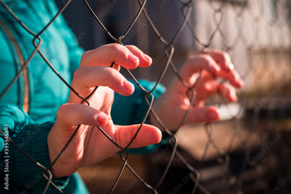 Close-up of a woman in a jacket holding her hands behind a mesh fence Close-up of a woman in a jacket holding her hands behind a mesh fence