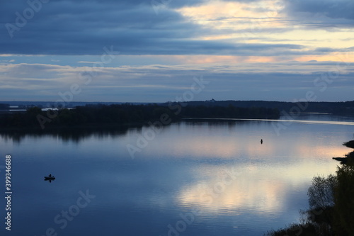 Fishing at dawn.Colorful blue lake landscape with a reflection of the sky and clouds with pink hues on the surface of the water and a man in a boat in the center.Beautiful panoramic view of the river