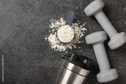 Whey protein powder, shaker and dumbbells on black photo