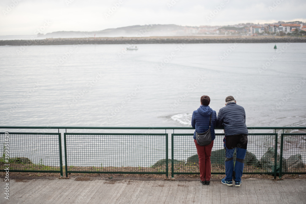 una pareja de personas mirando el mar apoyados en una barandilla. 