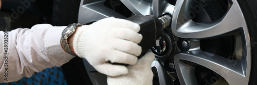 Fotografie Close up of male hands in white gloves using impact wrench while installing car