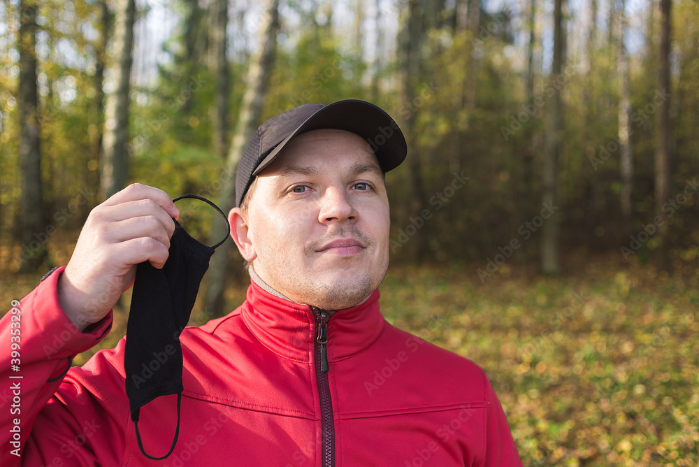 Obraz premium man outdoors takes off the mask from coronavirus. Man in outdoors takes off a black mask from coronavirus.
