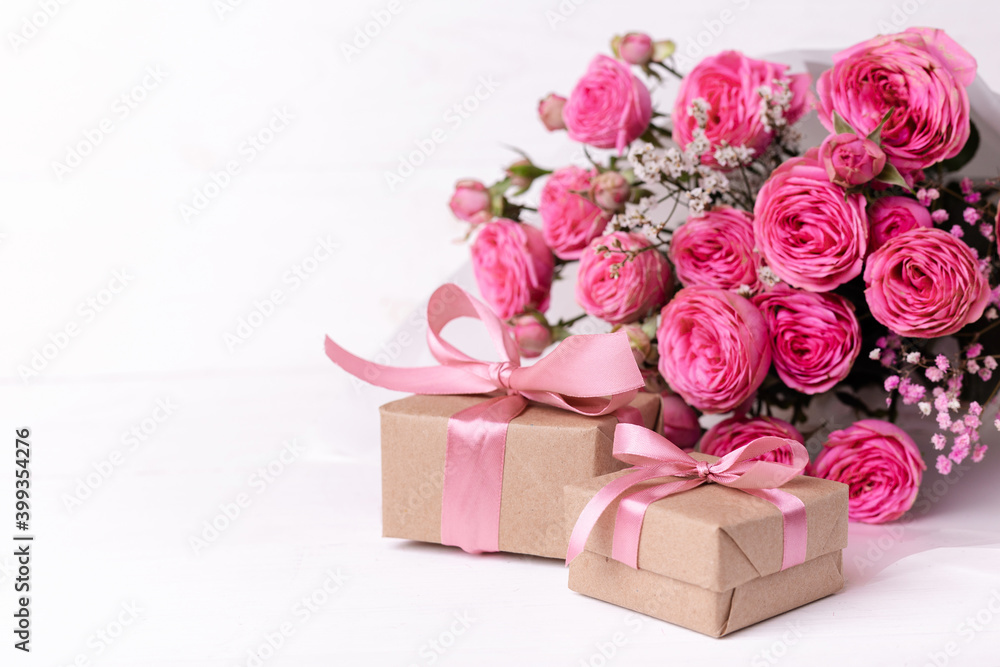 Fresh pastel soft pink roses, and gift boxes wrapped in kraft papper with ribbons on white wooden table. Fresh pastel soft pink roses, and gift boxes wrapped in kraft papper with ribbons on white wooden table.