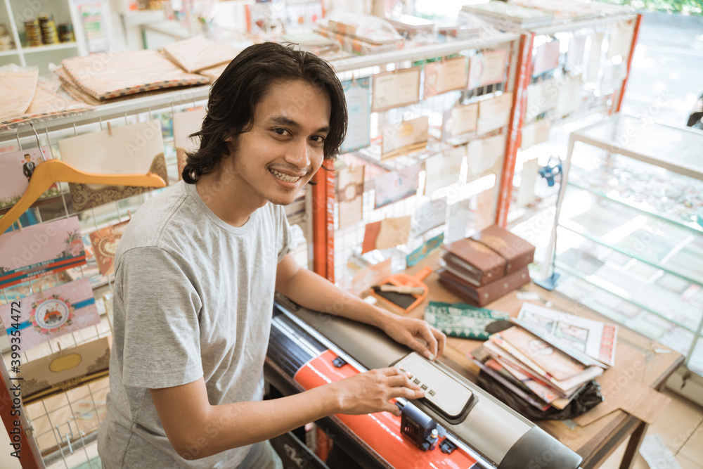 Young male entrepreneur Making sticker paper by machine working in a stationery shop.