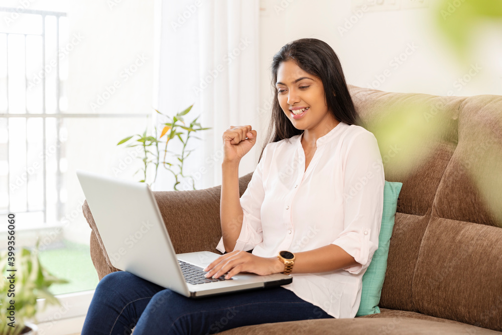 Cheerful pretty young woman working in laptop on sofa at home Cheerful pretty young woman working in laptop on sofa at home