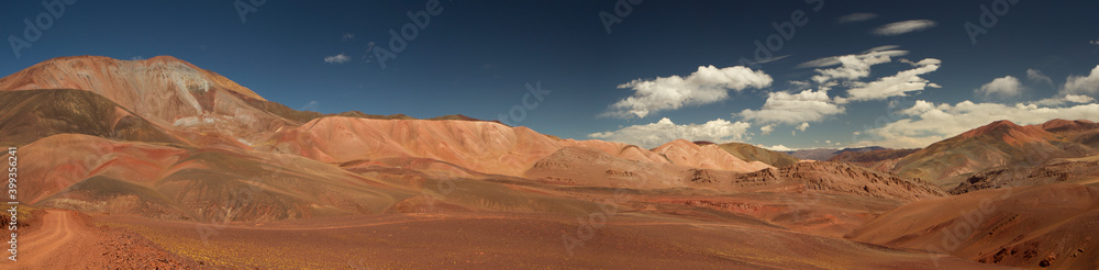 Traveling across the volcanic Andes desert very high in the cordillera. View of the dirt road along the dry valley. The brown land, yellow grasses, and colorful mountains under a beautiful sky.