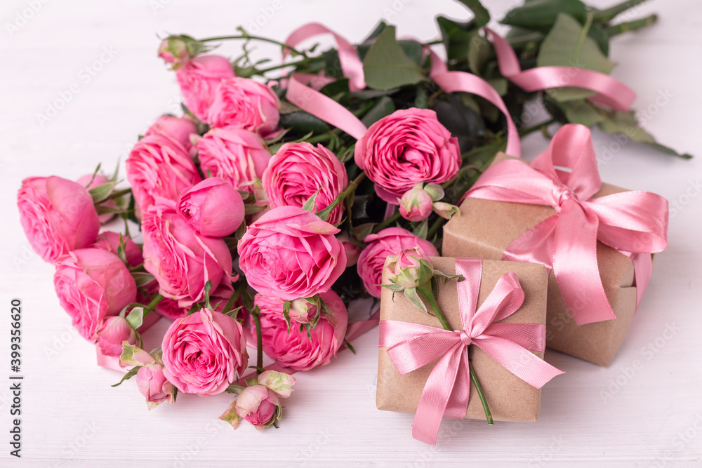 Fresh pastel soft pink roses, and gift boxes wrapped in kraft papper with ribbons on white wooden table.