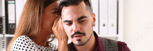 Foto Cheerful female worker telling gossip to male colleague in office