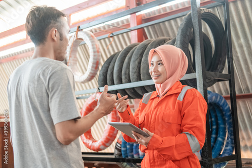 veiled female mechanics use digital tablets while chatting with male consumers standing in the background of a tire rack