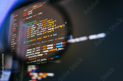 Program code on computer display in magnifying glass. Close-up photo