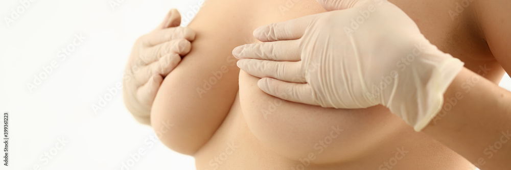 Close up of nude lady in sterile gloves placing hands on breast before plastic surgery Close up of nude lady in sterile gloves placing hands on breast before plastic surgery