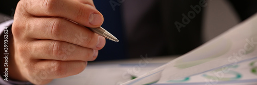 Close up of young man with pen in hand working with documents, financial charts and graphs in office