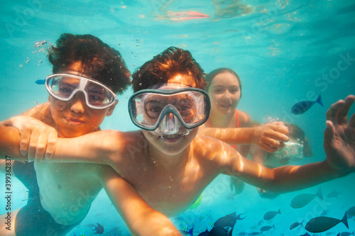 Two happy boys in scuba mask dive underwater with friends in sea among fish smile and play © Sergey Novikov
