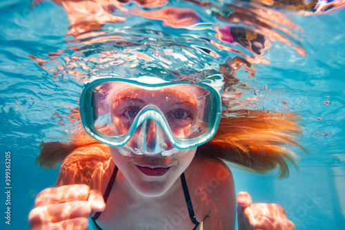 Beautiful underwater close-up portrait of the smiling little girl with long hairs wearing scuba mask