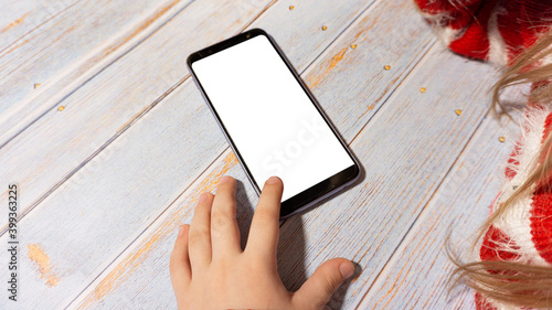 The child is sitting at a table with a phone with a white screen. A girl with a phone layout. In new year's clothing. New Year