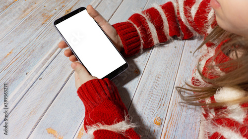 The child is sitting at a table with a phone with a white screen. A girl with a phone layout. In new year's clothing. New Year