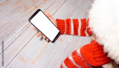 The child is sitting at a table with a phone with a white screen. A girl with a phone layout. In new year's clothing. New Year
