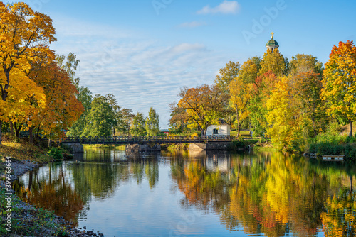 Autumn colored trees along a river in Sweden, with a bridge crossing the water and a church tower in the distance