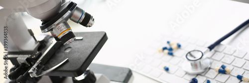Close up of white table with laboratory optical microscope, pharmaceutical drugs, keyboard and medical device for listening to internal sounds of body