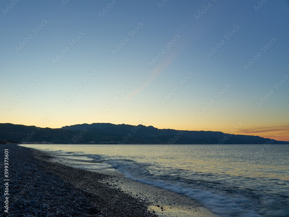Blurred waves on a pebble beach at sunset in Crete.
