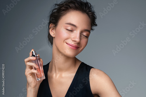 Woman with bottle of perfume. Photo of woman with perfect makeup on gray background. Beauty concept