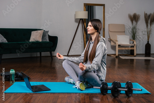 Young woman doing yoga exercises at home in a modern liiving room while watching online video lesson