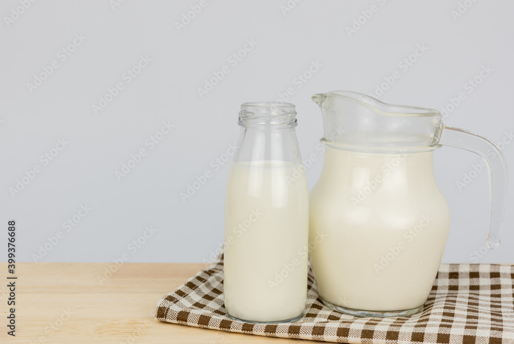 A jug and bottle of milk glass on a wooden table on background..Raw milk is high in calcium and protein to drink for all ages..Milk consumption nutritious and healthy dairy products concept.. A jug and bottle of milk glass on a wooden table on background..Raw milk is high in calcium and protein to drink for all ages..Milk consumption nutritious and healthy dairy products concept..