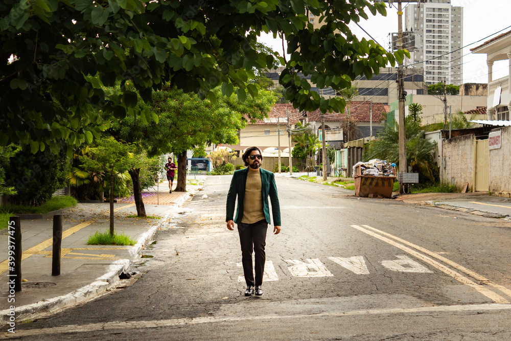 Homem elegante, usando óculos de sol e blazer, caminhando na rua.