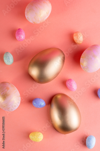 Trendy Easter background with Gold and colored Easter eggs on a light coral color background with copy space. Top view still life. Easter concept.