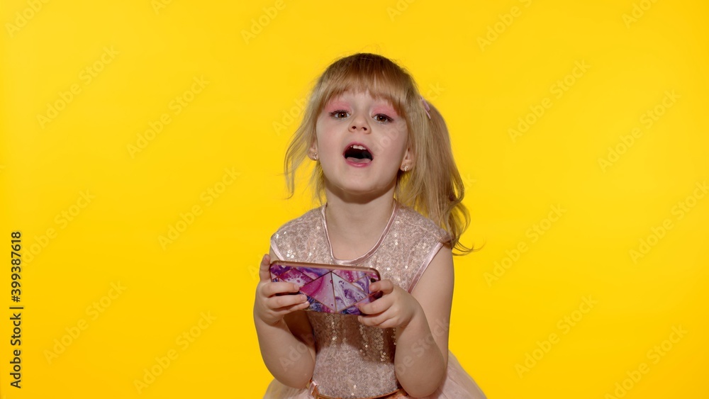 Little girl using smartphone. Portrait of child texting on smartphone. Kid enthusiastically playing games on mobile phone isolated on yellow background in studio. Technology for children