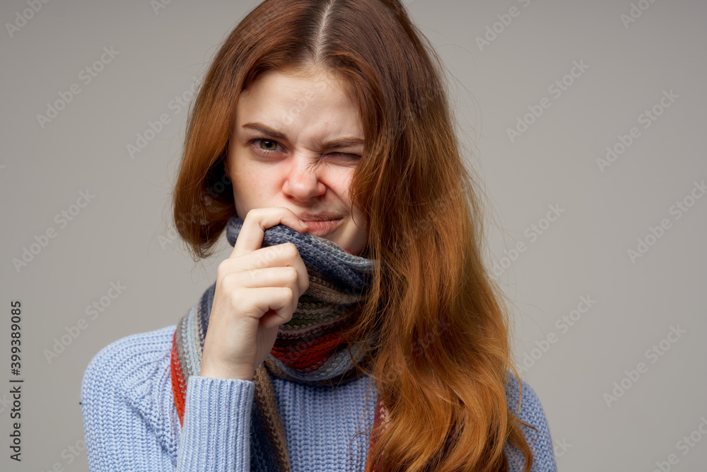 woman with a runny nose touches her head with her hands on a gray background portrait close-up
