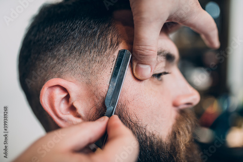 Young good looking hipste man visiting barber shop. Trendy and stylish beard styling and cut.