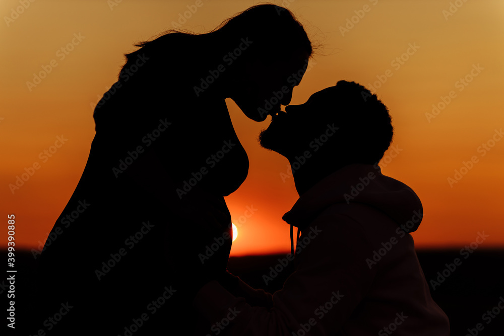 Silhouettes of lovely couple, beautiful woman kiss handsome man at sunset, enjoy tender moments, caring husband and loving wife spend time together, weekends outdoors concept