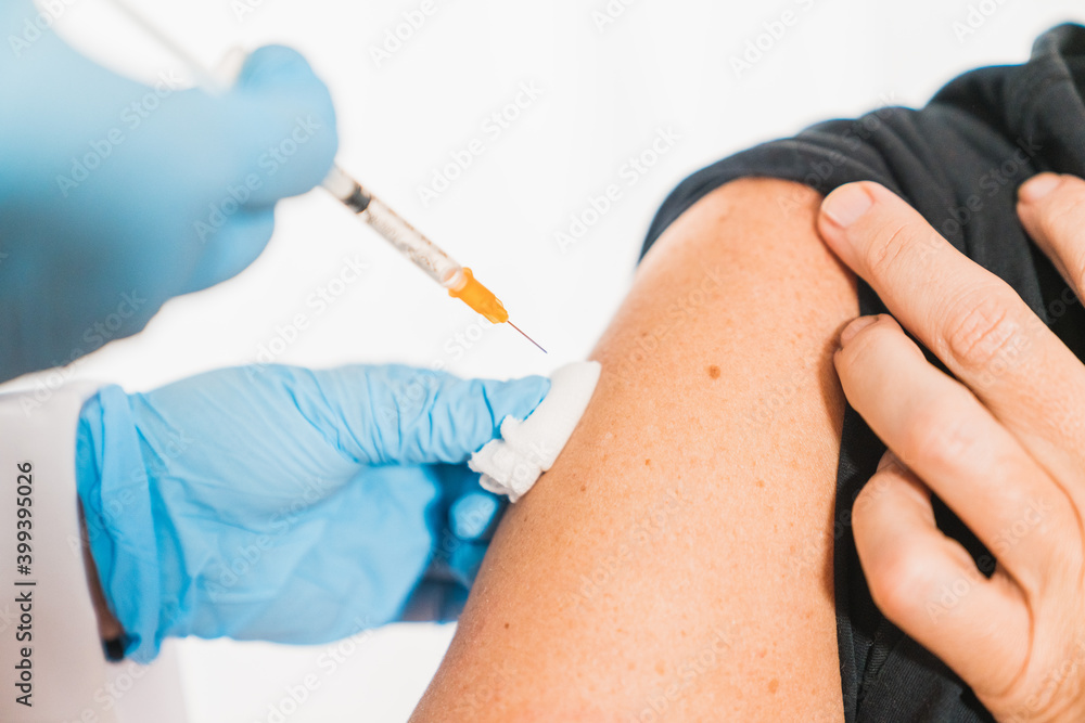 Putting a vaccine on a man's shoulder. Flu vaccine. Coronavirus vaccine. The female doctor vaccinated or syringe to injection to the young patient. Medical healthcare concept Putting a vaccine on a man's shoulder. Flu vaccine. Coronavirus vaccine. The female doctor vaccinated or syringe to injection to the young patient. Medical healthcare concept