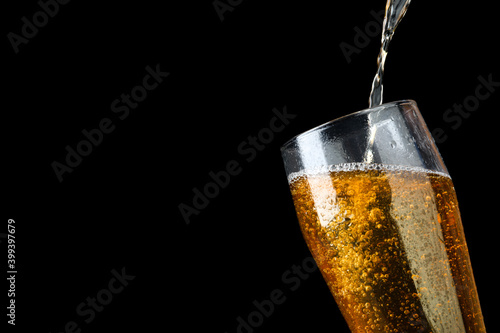 Pouring cold tasty beer into glass on black background, closeup. Space for text