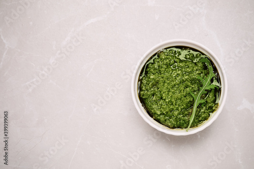 Bowl of tasty arugula pesto on light table, top view. Space for text