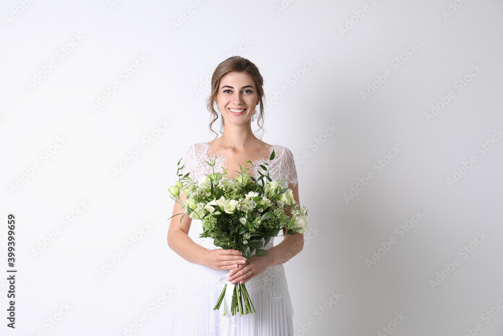 Young bride wearing wedding dress with beautiful bouquet on light background Young bride wearing wedding dress with beautiful bouquet on light background